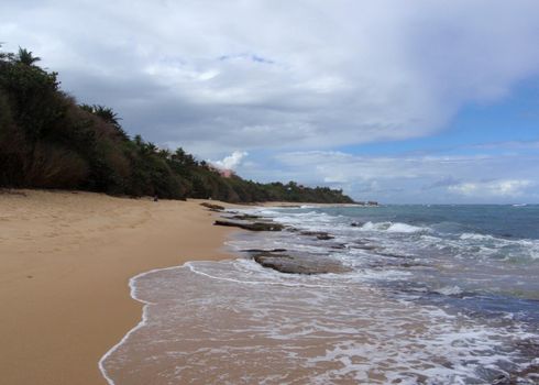 Beach rocks in the water and foot prints in the sand, San Juan, Puerto Rico on a beautiful day.