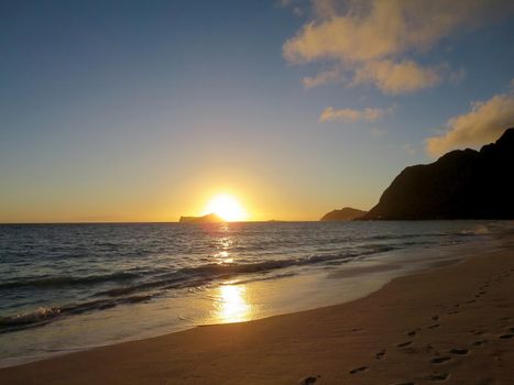 Early Morning Sunrise on Waimanalo Beach over Rabbit Island bursting over the island on Oahu, Hawaii.  With Lighthouse on mountain in distance.