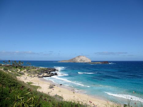 People play at the beach and in surf with view of Rabbit and Rock islands on a clear day at Makapuu Beach Park, Oahu, Hawaii.                              