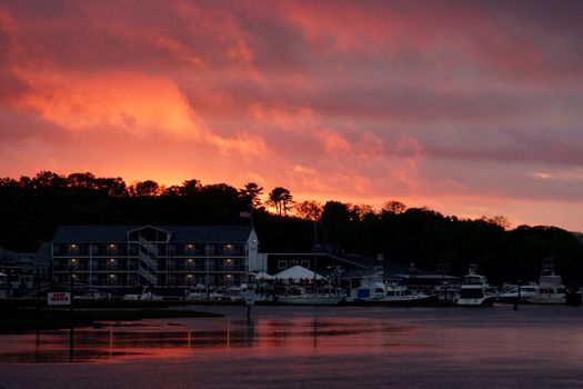 Sunset over Blynman Canal reflects on the water with boats and buildings with trees behind them in  Gloucester, Massachusetts.