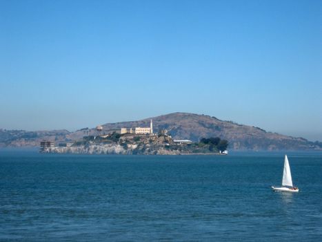 Alcatraz Island on a nice Day with a sail boat in front of it and Angel Island in the distance behind it. 