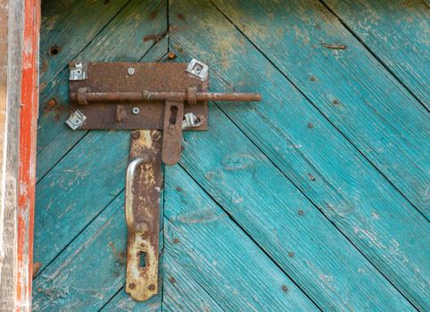 Metal rusty deadbolt and doorknob on old worn green door.