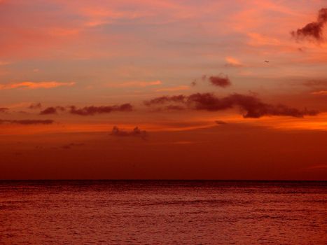 Red light of dusk over the ocean and sky as plane flies in the air on Oahu, Hawaii.