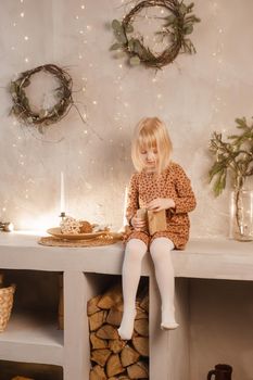 A girl is playing on Christmas Eve in a beautiful house decorated for the New Year holidays. Scandinavian-style interior with live fir trees and a wooden staircase.