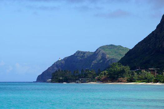 Waimanalo beach, bay, and Makapuu Point with Makapu'u Lighthouse visible on cliffside mountain on windward coast of Oahu, Hawaii and boat in the water.