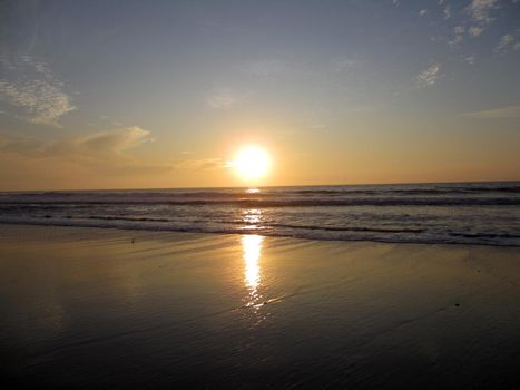 Sunset over ocean waves crashing along the beach on Half Moon Bay in California with sunlight reflecting on the water.                               