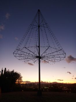  the Kaimuki Christmas tree (Metal Light Tree) on top Pu'u O Kaimuki (also known as Menehune Hill) at dusk on with cityscape of Oahu, Hawaii.