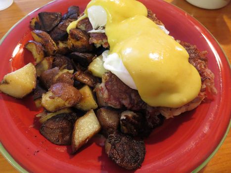 Eggs Florentine with two poached eggs, English muffins, corn beef hash, and potatoes on a red plate