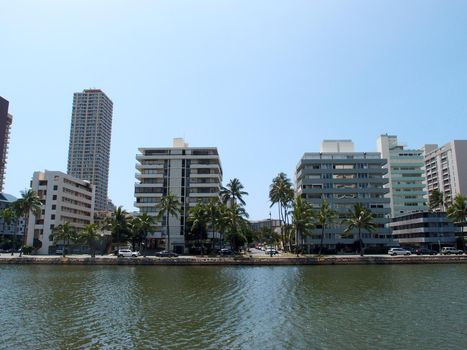 Ala Wai Canel in Waikiki on the island of Oahu in the state of Hawaii.   With walking path, trees, and tall buildings lining street next to canel. 