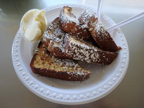 Sweet Bread French Toast - 5 Pieces with cup of butter on a plastic plate with plastic knife on a metal table.