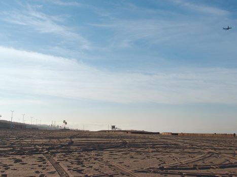 Tire tracks in the sand on an empty Dockweiler Beach State Park, Playa Del Rey in LA, California in the morning with plane flying in the air.