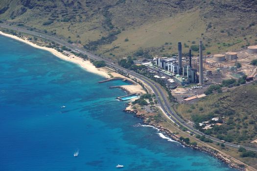 Aerial view of Kahe Point Power Plant sits along the ocean with highway road and boats in the water on the ewa side of Oahu, Hawaii.