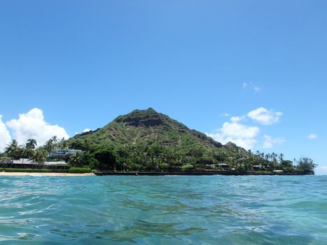 Beach and Makalei Beach Park with seawall, coconut trees, homes, and Diamond Head Crater in the distance on Oahu, Hawaii viewed from the water.