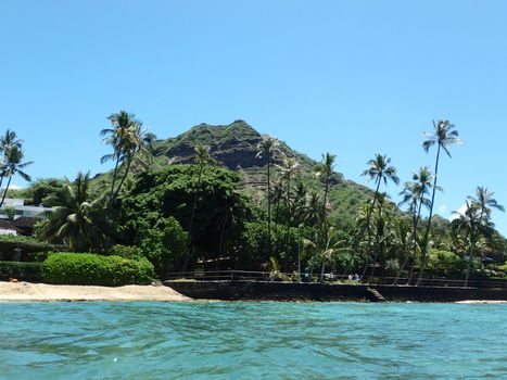 Beach and Makalei Beach Park with seawall, coconut trees, and Diamond Head Crater in the distance on Oahu, Hawaii viewed from the water. 