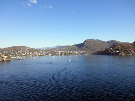 view waters of Zihuatanejo Harbor with boats in water and buildings on hillside in Mexico.