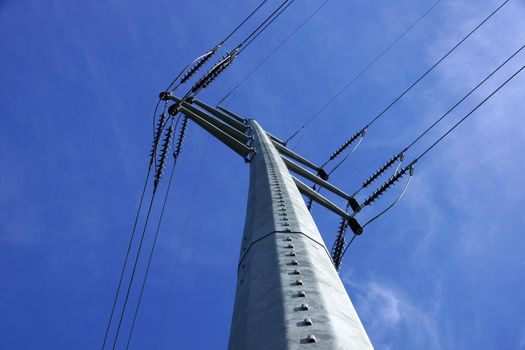 High Voltage Power Lines intersect at a large metal Utility pole in Maine against a blue sky.