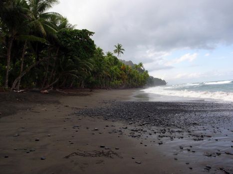 The Hawaiian word 'Aloha' written in the Sand on Tropical Beach with rocks and coconut trees lining the shore.