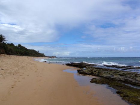 Beach with rocks in the water and foot prints in the sand, San Juan, Puerto Rico on a beautiful day with waves lapping on the beach.