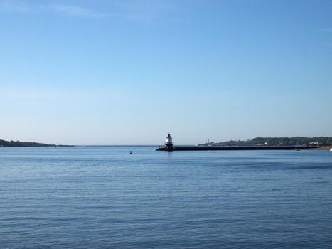 Lighthouse "Bug Light" at end of jetty rocky cove with boat and historic Portland Head Light visible leading to the ocean on a beautiful day.