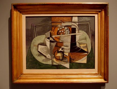 Le Tapis Vert, 1929, Georges Braque -  In this still life, flat planes of neutral color advance and recede against the picture plane, emphasizing its two-dimensionality even as they overlap, merge, and collide to suggest three-dimensional objects arranged on a precariously tipped table. Analytical Cubism's dissolution of form has been replaced by the build-up of shapes into an easily readable composition that represents rather than replicates nature, as indicated in the trompe l'oeil frame that just barely contains the grapes, glass, apple, pipe, and bowl within its borders.