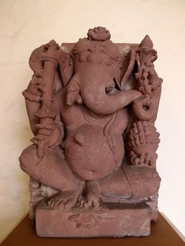 Seated Ganesha, made in India of sandstone in 9th Century at the Honolulu Art Musuem.  Among the objects Ganesha holds is his own tusk.  One story recounts that after falling off of his rat vehicle, Ganesha's stomach burst open and all of the sweetmeats he had eaten fell out.  He picked them up and put them back inside, securing his stomach by tying a snake around it.  The moon, having watched this event, burst out laughing.  In his fury, Ganesha broke off his tusk and threw it at the moon, causing a temporary period of darkness, explaining the moon's cycle of waxing and waning.