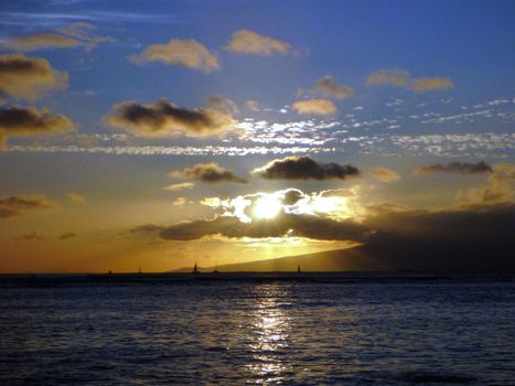 Dramatic Sunset through the clouds over the Pacific ocean with boats sailing on the water of Waikiki on Oahu, Hawaii.