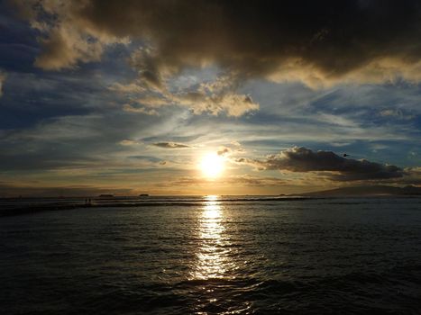 Sunset over the Waters of Waikiki with boats in the ocean and helicopter in the air as the sunlight reflects on the waves on Oahu, Hawaii.