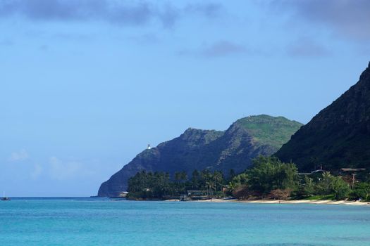 Waimanalo beach, bay, and Makapuu Point with Makapu'u Lighthouse visible on cliffside mountain on windward coast of Oahu, Hawaii and boat in the water.