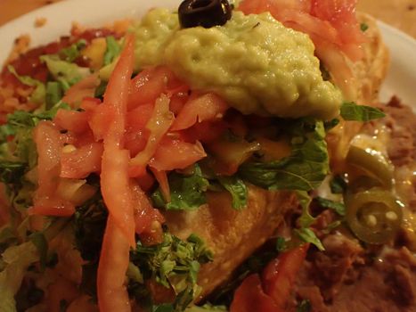 Close-up of Chimichanga topped with salsa, guacamole with spanish rice, beans, on table.