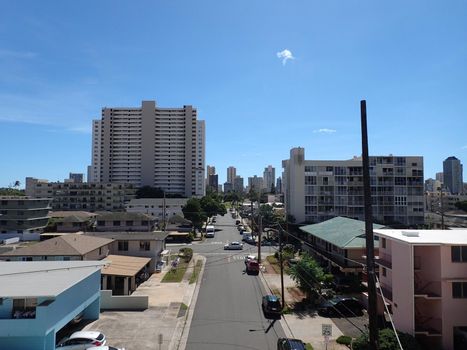 Kapahulu town scape featuring street with parked cars, homes, and condo buildings with Waikiki Hotels in the background in Honolulu, Hawaii.