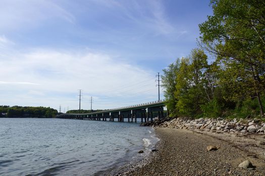 Rocky beach leading to a Bridge and Power lines cross waterway connecting Cousins Island to the mainland of Maine.