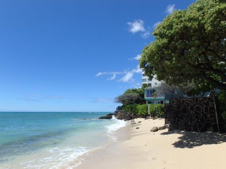 Makalei Beach with waves lapping, napakaa, lava rock wall and small hotels along the shore on a wonderful day in Oahu, Hawaii.