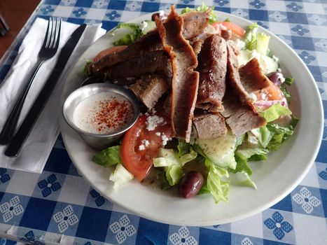 Gyros Salad - Hot slices of beef and lamb topped tzatziki sauce on a bed of romaine lettuce, onions, tomatoes, cucumbers, kalamata olives, and feta cheese.