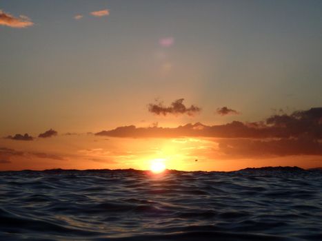 Dramatic lighting the sky and ocean during sunsets with light reflecting on ocean waves moving with parasailer on the water in the distance off Waikiki with clouds on Oahu, Hawaii.