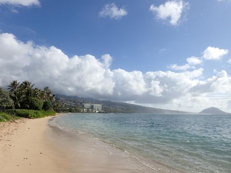 Sandy shoreline of Kahala Beach, hotel, and the southern coastline of Oahu, Hawaii on a beautiful day.