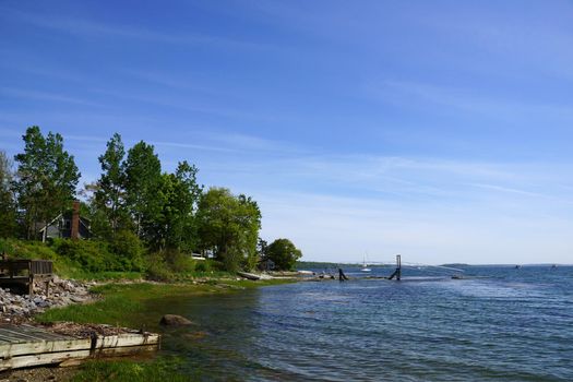 Rocky coastline with pier in distance and green trees on Littlejohn Island, Yarmouth, Maine