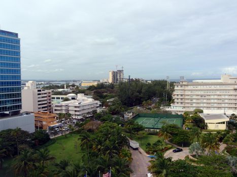 Entrance to Hotel Grounds with Tennis Court, surrounded by modern buildings, and buildings under construction on a cloudy day.  Taken from High Up In San Juan, Puerto Rico.