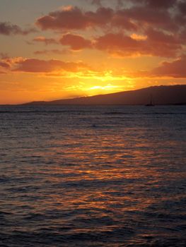 dramatic lighting the sky after Sun sets behind Waianae mountains with light reflecting on  ocean with boats sailing on the water  off Waikiki on Oahu, Hawaii.