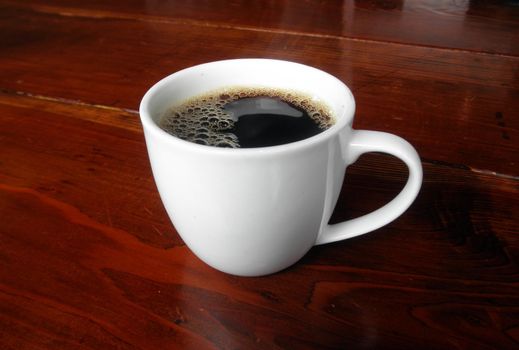 White Mug Full of Bubbly Coffee on a wooden table.     