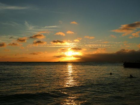 dramatic Sunset on Kaimana Beach over the ocean with boats sailing on the water on Oahu, Hawaii.