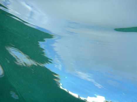 Looking through ocean water at blue sky with water ripples and air bubbles from underwater.