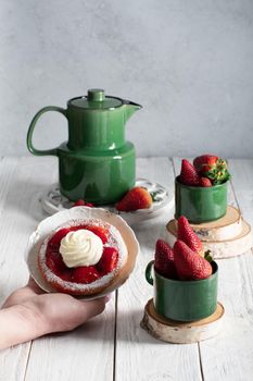 Fruit still life with strawberries and green tea set, strawberry cake with cream sweet dessert, female hand breaks off a piece of cake with a dessert fork. High quality photo