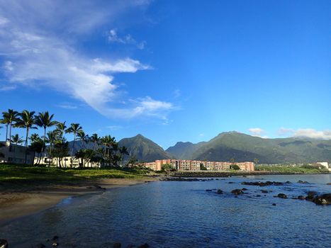 Kahului Bay with Hotel, coconut trees, and Iao Valley and surrounding mountains in the distance on West Maui on a beautiful day.