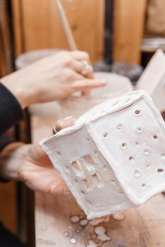 A master ceramist holds a clay product in his hands. Making a ceramic candle holder from clay. The process of coating the candlestick with glaze. Close-up.