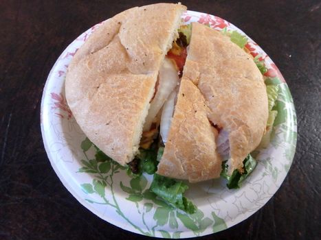 Taro Burger on homemade focaccia bread with lettuce, tomatoes and onions on a paper plate.