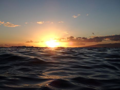 Dramatic lighting the sky and ocean during sunsets with light reflecting on ocean waves moving with boats sailing on the water off Waikiki with clouds on Oahu, Hawaii. 