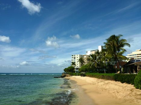 Makalei Beach with waves lapping, napakaa, lava rock wall and small hotels along the shore on a wonderful day in Oahu, Hawaii. 