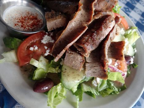 Gyros Salad - Hot slices of beef and lamb topped tzatziki sauce on a bed of romaine lettuce, onions, tomatoes, cucumbers, kalamata olives, and feta cheese.