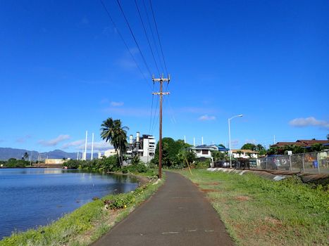 Pearl Harbor Bike Path along the water with Power lines overhead leading to power plant in the distance on Oahu, Hawaii.