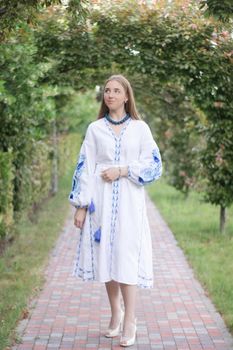 Portrait of young Ukrainian woman dressed in blue national traditional embroidered shirt in park outdoor.